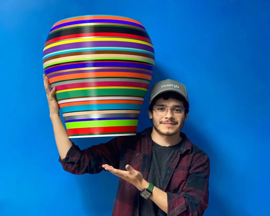 A person holding a large 3D-printed planter banded in many colors aloft in one hand